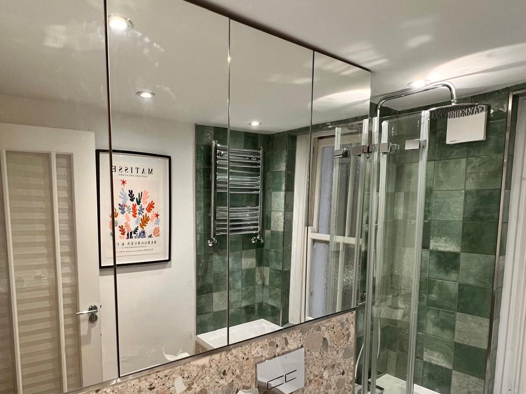 Mirrored bathroom cabinets above a basin with a rain shower beyond