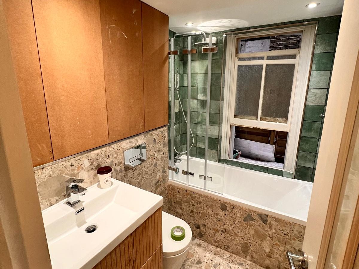 Bathroom with green wall tiles, terrazzo effect floor and a timber vanity unit