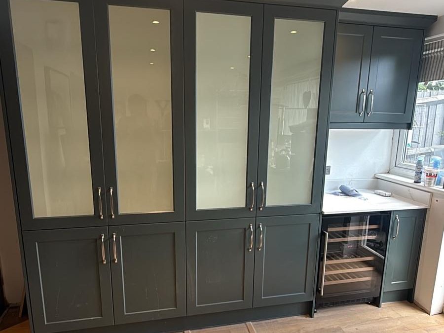 Dark green shaker units with glazed doors and an integrated wine cooler