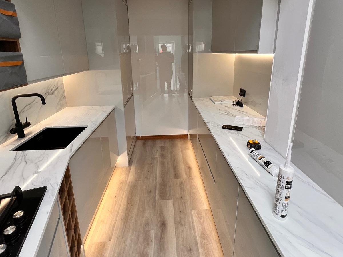 Galley kitchen with grey gloss units, marble effect worktops and plinth lighting