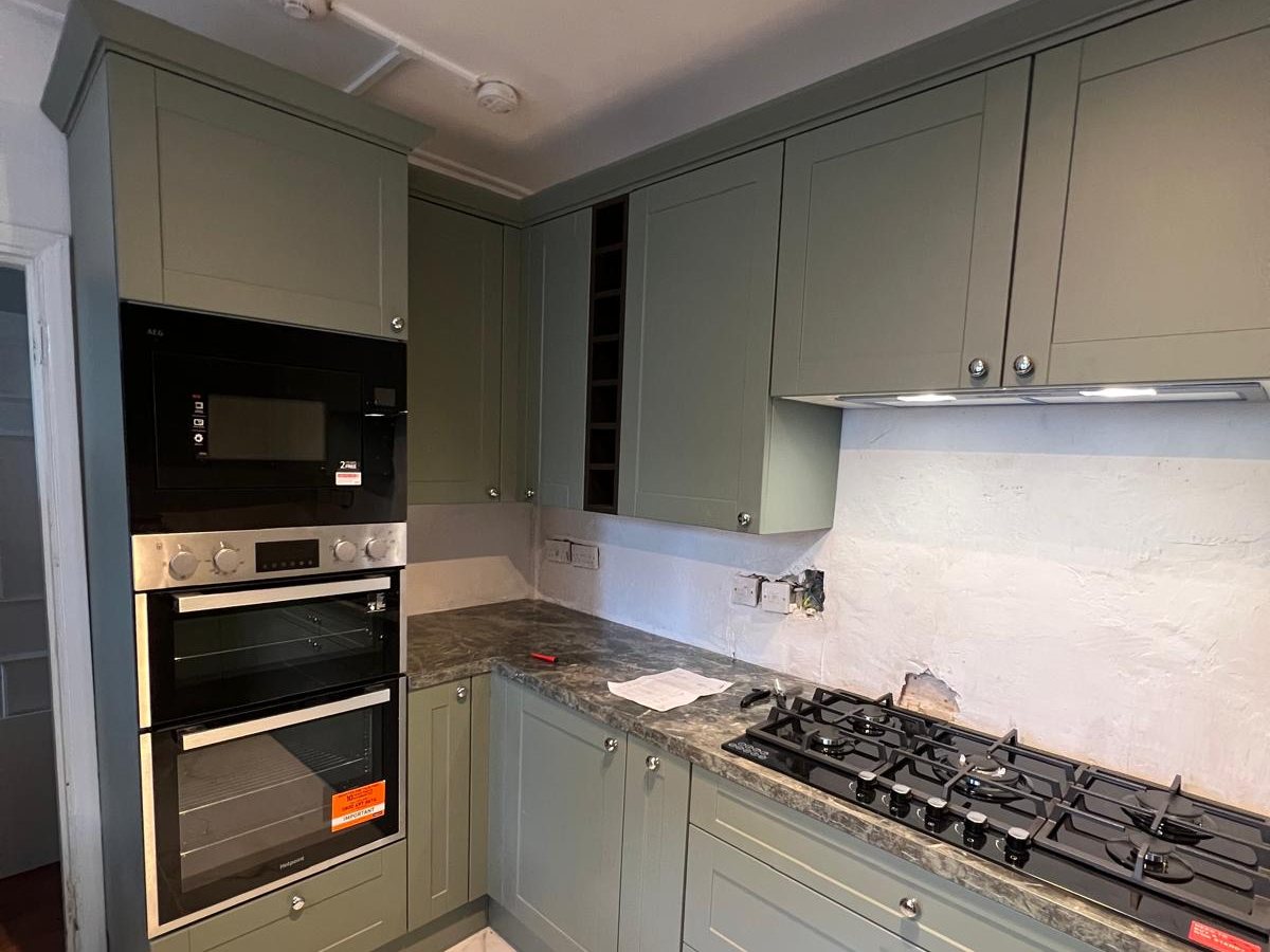 Sage green shaker kitchen with built in ovens and a gas hob